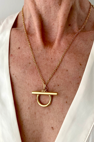 Ma Cocotte N54MAC Omega Necklace Gold necklace with a unique pendant on a person wearing a white garment.