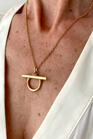 Ma Cocotte N54MAC Omega Necklace Gold necklace with a unique pendant on a person wearing a white shirt.