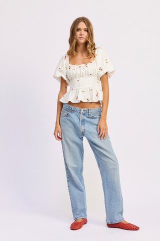 Woman wearing a white blouse and light blue jeans on a white background En Saison Strawberry Kiss Embroidered Peplum Top