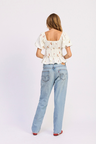 Woman wearing a white blouse with floral patterns and light blue jeans on a white background En Saison Strawberry Kiss Embroidered Peplum Top