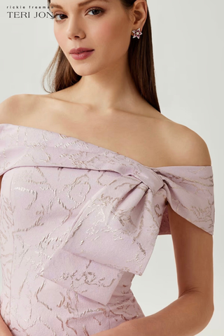 Teri Jon 266012 Jacquard Asymmetrical Off The Shoulder Side Bow Godet Gown Woman wearing a light purple off-shoulder dress with intricate detailing on a plain background
