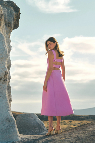 Leo & Ugo KER063 Nina Open Back Midi Dress Woman in a pink dress standing near a rock formation with a cloudy sky.