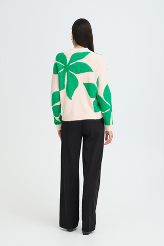 Person wearing a cream sweater with green leaf patterns and black pants on a white background b. young BYOmea Flower Sweater