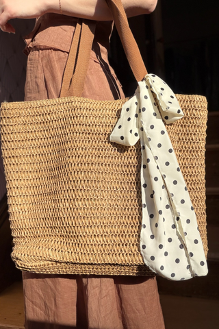 Leo & Ugo KEBH086 Polka Dot Trim Hat & Bag Combo Woven straw bag with a polka dot ribbon held by a person wearing brown pants.