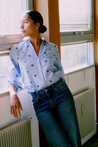 Woman wearing a light blue shirt with dark patterns and jeans, standing by a window. b. young BYFabienne Long Sleeve Shirt