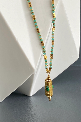 Ma Cocotte N37MAC Khiva Necklace Necklace with gold and turquoise beads on a white geometric background