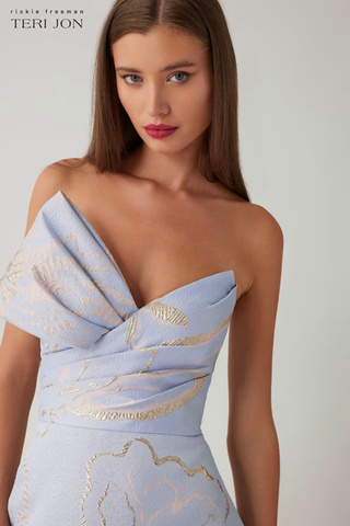 Teri Jon 266025 Metallic Jacquard Strapless Side Bow A Line Skirt Gown Woman wearing a light blue strapless dress with gold accents on a plain background