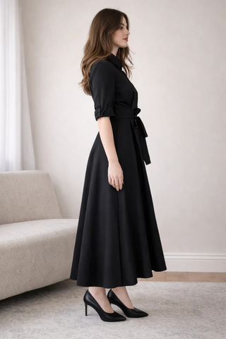 Leo & Ugo EER620 Black Tie-Waist Midi Shirt Dress Woman wearing a black dress standing in a room with a neutral color scheme.