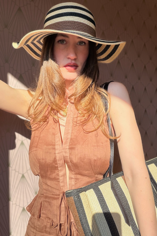 Leo & Ugo KEBH088 Neutral Striped Hat & Bag Combo Woman wearing a wide-brimmed hat and holding a bag, standing against a textured wall.