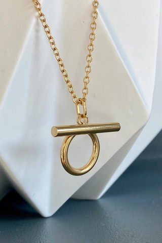 Ma Cocotte N54MAC Omega Necklace Gold necklace with a circular pendant on a white geometric stand.