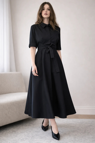Leo & Ugo EER620 Black Tie-Waist Midi Shirt Dress Woman wearing a black dress in a room with a beige sofa and white walls.