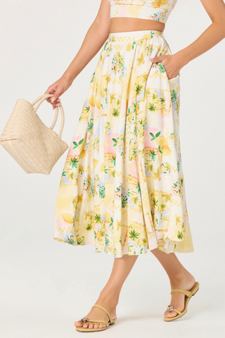 Woman wearing a yellow floral dress holding a straw bag on a white background