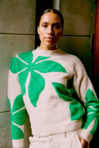 Person wearing a beige sweater with green leaf patterns against a neutral background b. young BYOmea Flower Sweater