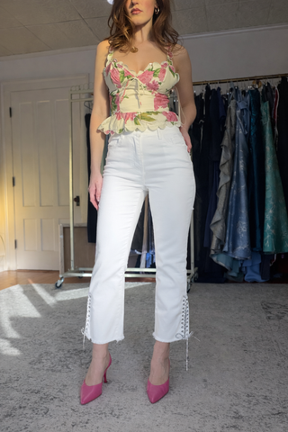 oo la la M10129 Rhinestone Shoelace Bottom Crop Jeans Woman wearing a floral top and white pants with lace details in a clothing store.