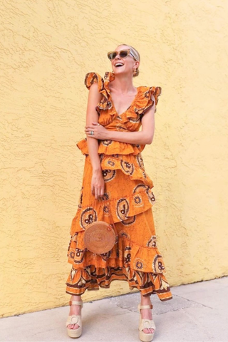 Love the Label Gigi Dress Woman in an orange patterned dress standing against a yellow wall